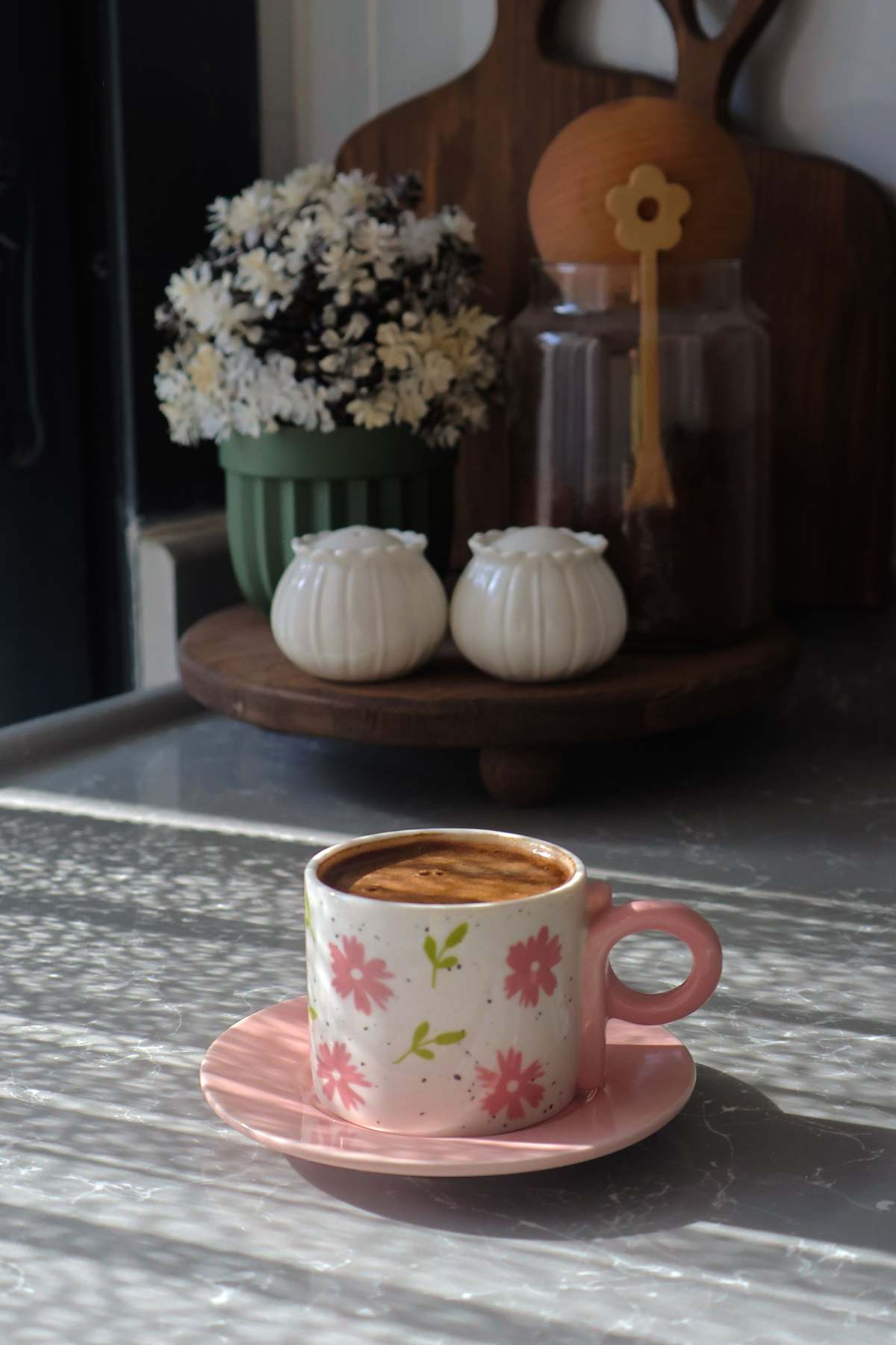A floral mug of coffee on a saucer on a sunlit kitchen worktop